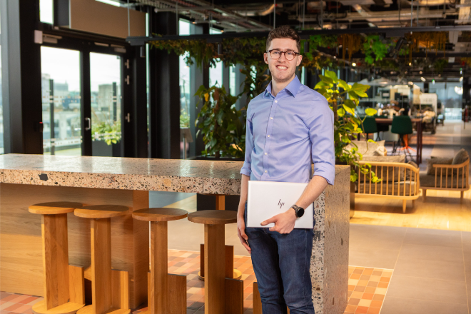 Young man wearing glasses and holding a laptop.