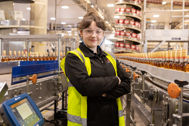 Smiling young woman wearing a hi-viz vest and safety goggles.