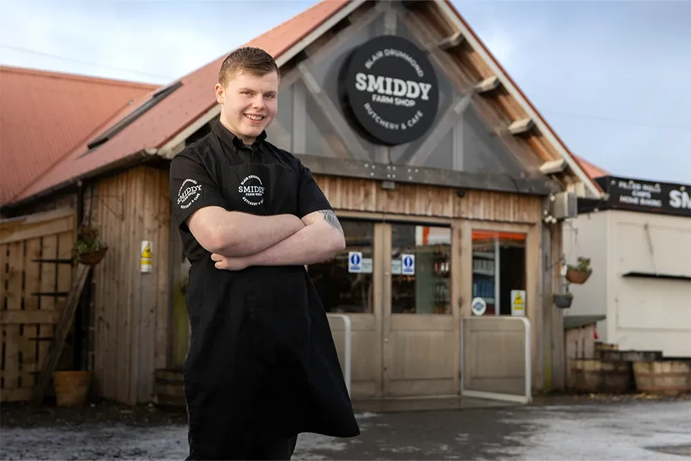 Young smiling man in catering clothing, outside shop with sign 'Smiddy Farm Shop'
