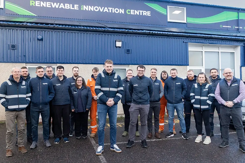 Group of smiling employees outside building with sign 'Renewable Innovation Centre'